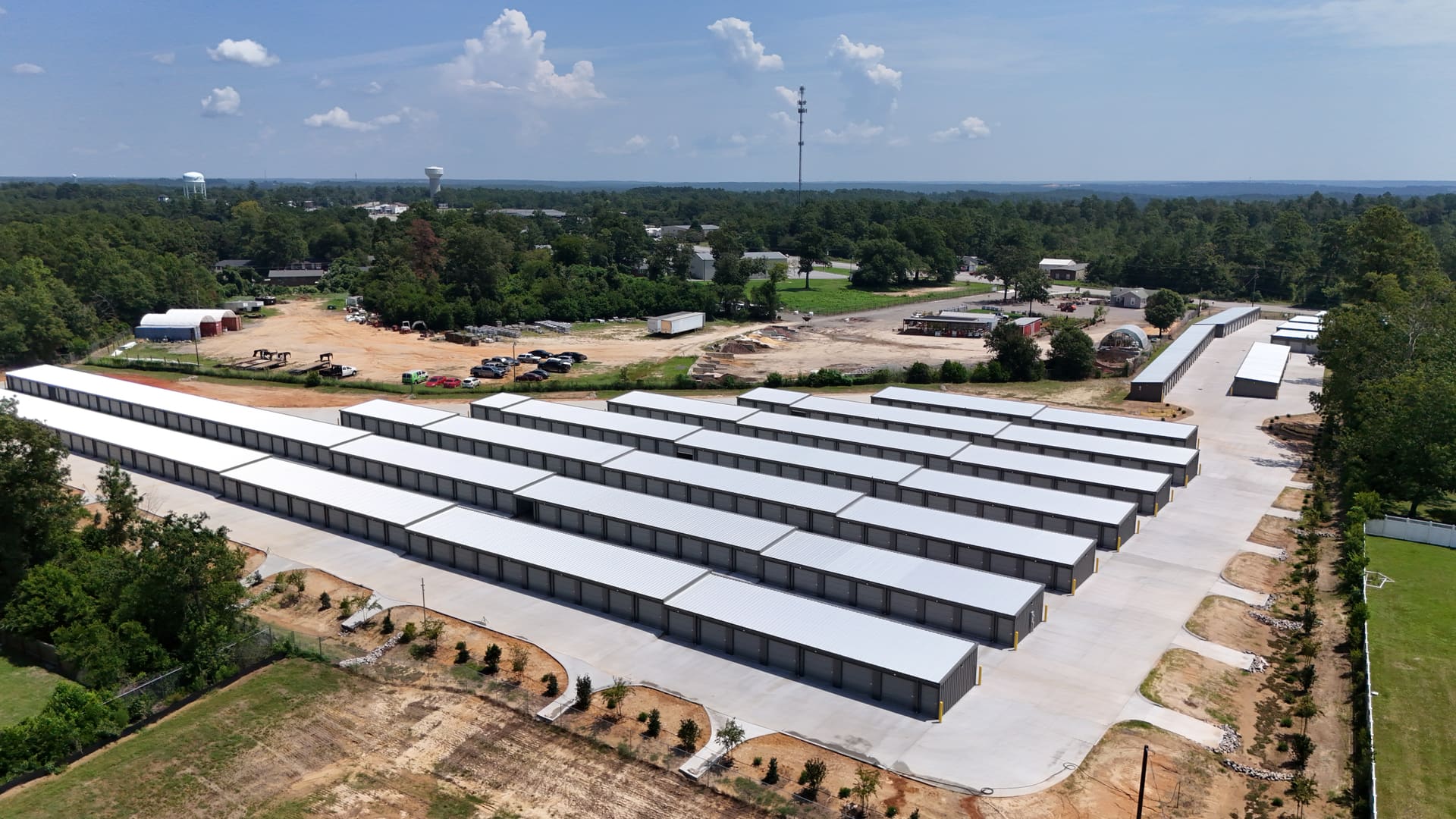 Aerial view of My Storage: row after row of drive-up storage buildings with white roofs and grey roll-up doors, on new concrete, with the tree line and horizon of Belvedere, South Carolina behind them.