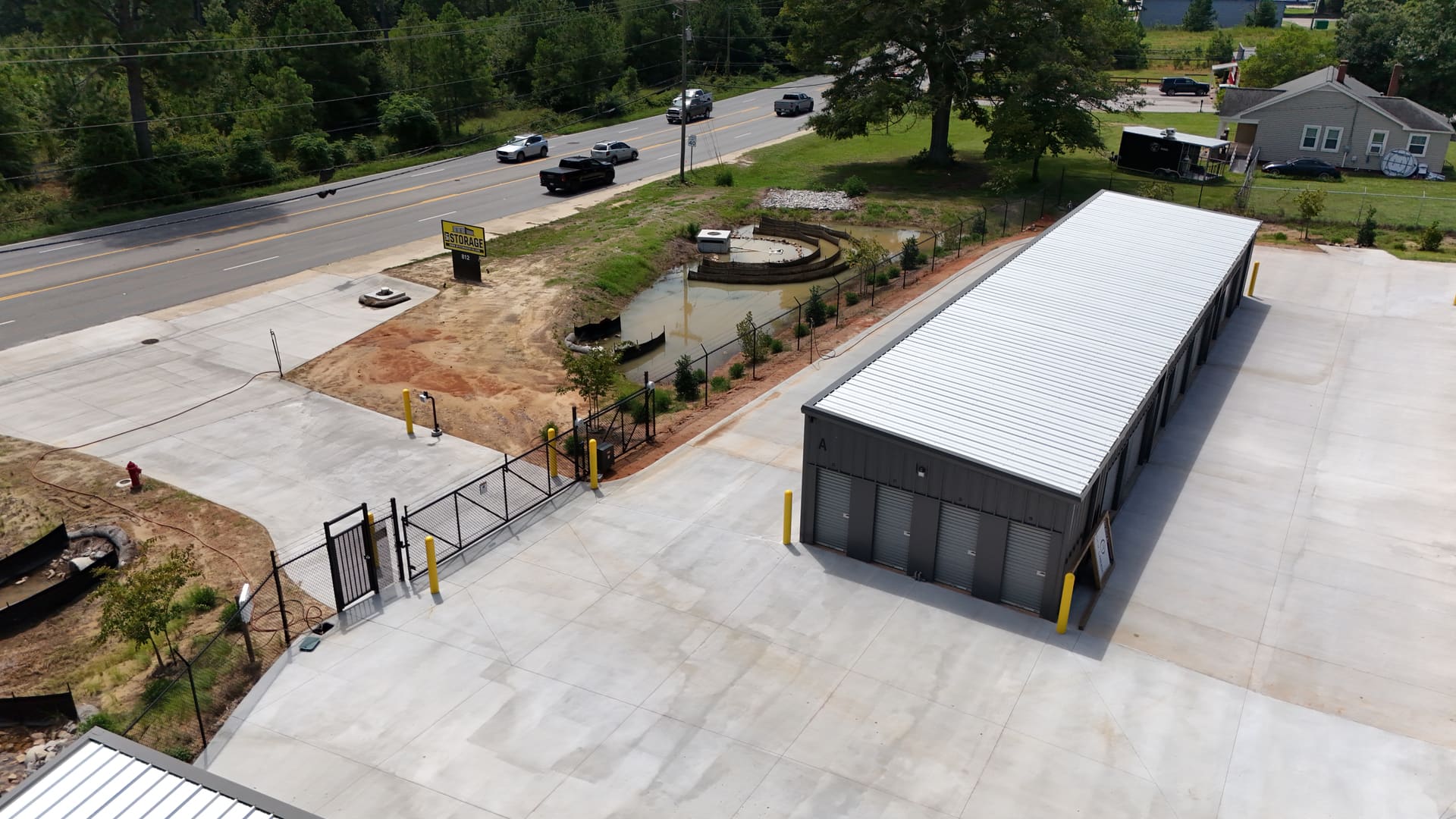 The entrance to My Storage from Edgefield Road: the road sign at the kerb, the sliding gate in the black perimeter fence, the concrete apron, and the first storage building standing just inside.