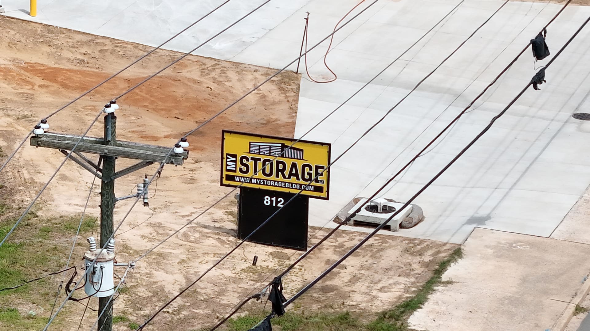 My Storage's yellow and black road sign standing at the edge of Edgefield Road, with the street number 812 on the black panel beneath it and the site's concrete entrance apron behind.