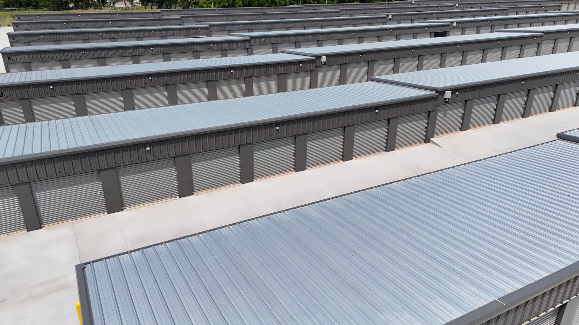 Rows of individual grey roll-up doors at My Storage, with a letter painted at the end of each building and a number beside each door, and concrete drive aisles running between the rows.
